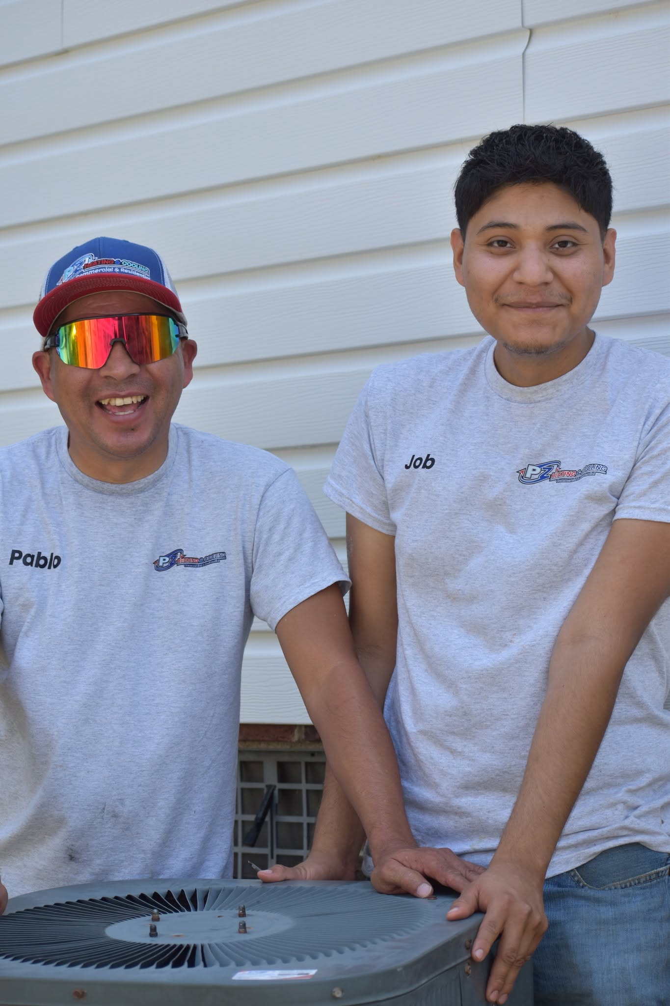 PZ Heating & Cooling technicians Pablo and Job beside a residential condenser unit