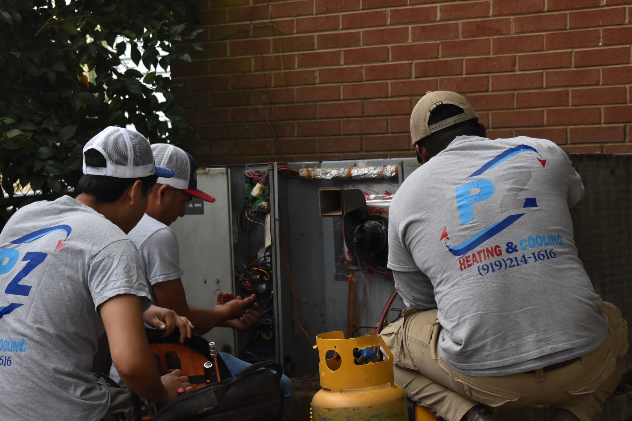Three PZ Heating & Cooling technicians working together on a rooftop HVAC unit
